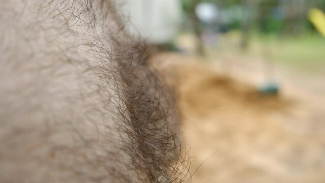 Close up of hairy male pale chest in profile or side view and very shadow depth of field while standing outdoor next to pile of sand.
