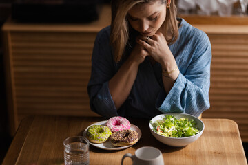 Young woman having diet, deciding between salad and donuts.