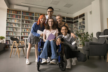 Multiethnic college student friends and classmate girl with disability posing in campus library,...