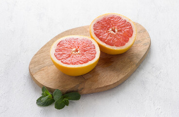 Wooden board with two halves of a grapefruit on a light gray background, top view