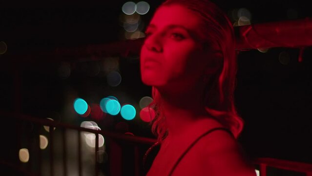 woman on the balcony of a flat at night with neon lights and the city in the backgroundwoman on the balcony of a flat at night with neon lights and the city in the background