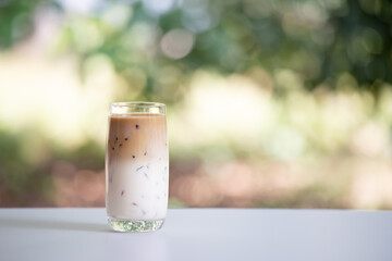 Iced coffee on white table, green background. Cold beverage in summer.