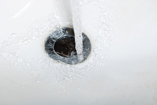 Drinking water falling down the drain, concept of water waste and lack of awareness. Close up open faucet pouring liquid