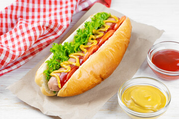Homemade Hot Dog with yellow mustard, ketchup, tomato and fresh salad leaves on white wooden background. Fast food, street food, american cuisine