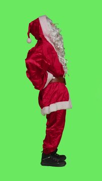 Vertical video Profile of santa suffers from back pain in studio, feeling unwell standing over full body greenscreen backdrop. Man portraying saint nick dealing with hurt spine during christmas eve