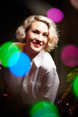 An elegant blonde girl in a white blouse in a room decorated for Christmas or new year with a background, tinsel and light garlands