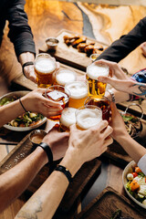 Friends cheering beer glasses on wooden table covered with delicious food - Top view of people having dinner party at bar restaurant - Food and beverage lifestyle concept - 619529539