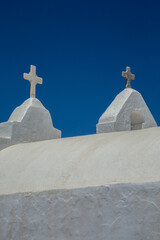 Old Mediterranean architecture white Greek church with two crosses, under the sun in Mykonos, Cyclades, Greece.
