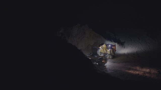 Excavator in action at the open mine pit at night. View of excavator flipping the bucket of yellow color loaded with ore into dumper truck, slow motion