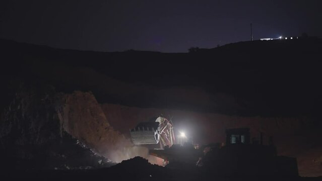 Work of trucks and the excavator in an open pit on gold mining at night, slow motion