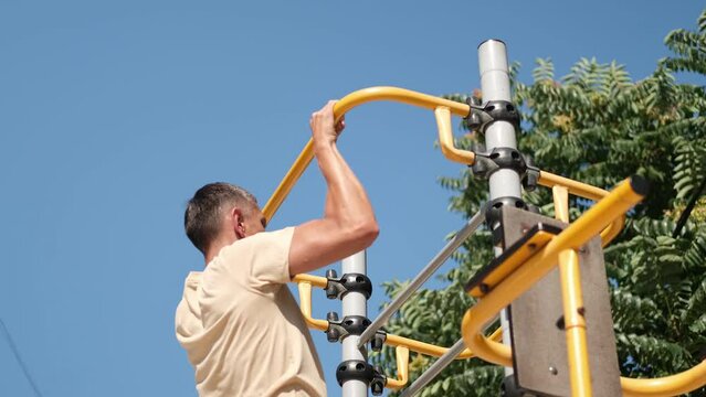 A man goes in for sports on the street. The guy pulls up on the crossbar on the street sports ground.