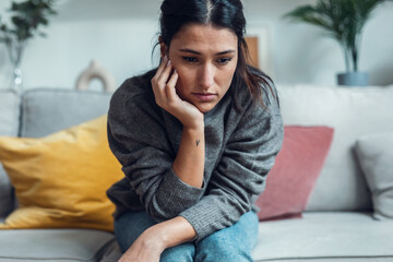 Worried depressed woman thinking while sitting on sofa in the living room at home.