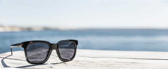 Fototapeta na wymiar Sonnenbrille af einem Holzdeck an der Küste