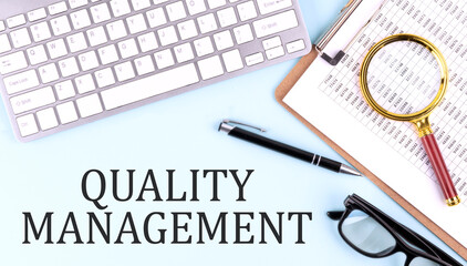 QUALITY MANAGEMENT text on blue background with keyboard and clipboard, business concept
