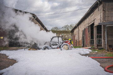 Die Feuerwehr nutzt Löschschaum um einen brennenden Radlader zu löschen, wobei es zu einer starken Rauchentwicklung kommt...Ein Schaumteppich ist am Boden zu sehen...28.03.2023