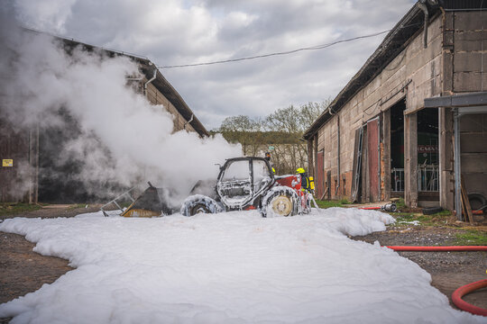Die Feuerwehr nutzt L&ouml;schschaum um einen brennenden Radlader zu l&ouml;schen, wobei es zu einer starken Rauchentwicklung kommt...Ein Schaumteppich ist am Boden zu sehen...28.03.2023