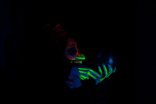 Woman make up as a catrina uses neon paint to simulate skeleton and kisses a skull day of the dead tradition and culture in Mexico day of the dead