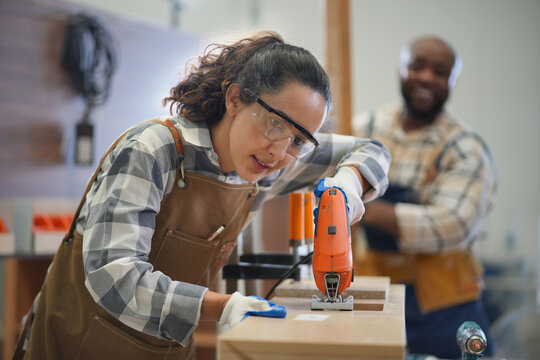 Young female capenter in apron working in carpentry woodworking workshop, Carpenter woman concept.