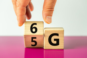 time for the 6G symbol. The hand rotates the wooden cube and changes the 5G sign to 6G. Concept, technology development, high speed communication network and 6g. Beautiful fuchsia and white background