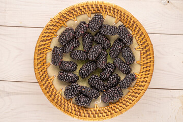 Several sweet blackberry berries with  ceramic plate on wooden table, macro, top view.