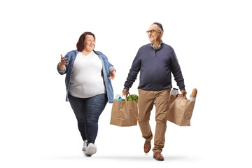 Full length portrait of a mature man with grocery bags walking with a corpulent young woman