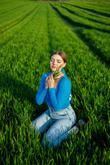 A smiling young woman is sitting in a spacious field on green grass.