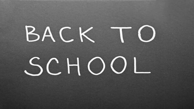 Back to school simple animation. Animation on black background. Stop motion animation. Handwritten text with white chalk on a blackboard. Monochrome. Concept of education. Hand-drawn simple font.