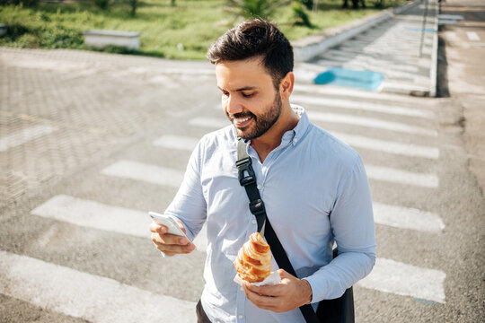 A businessman finding a moment of calm in the city, eating a croissant while using his cellphone
