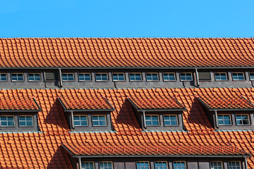 Attic windows in orange tiled roof against blue sky background