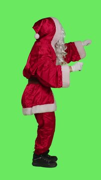 Vertical video Profile of santa choirmaster conducting band, conductor in winter seasonal costume accompany choir over full body greenscreen backdrop. Character pretends to be musical director