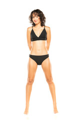 Young smiling exotic brunette woman in black bikini swimsuit posing on a white background. Front view.