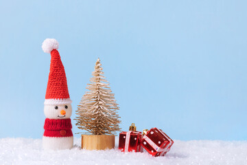 Knitted snowman in a red Christmas hat and sweater with two red gifts under the toy Christmas tree...