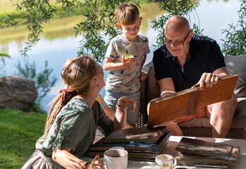 Grandpa with his grandchildren looking at old photo albums on outdoor terrace on a sunny summer day