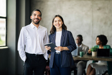 Middle Eastern Businessman And European Businesswoman Holding Tablet In Office