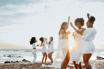 Group of carefree young women toasting wine glasses, dancing and having fun on the beach, having hen party at coastline