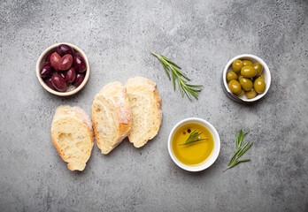Slices of fresh ciabatta, green and brown olives, olive oil with rosemary, olive tree branches on...