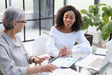Fototapeta premium Two business women smile while working together on a laptop at a table in the boardroom in the office