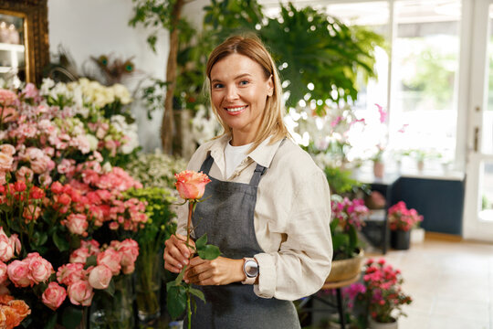 Woman florist flower shop owner hold rose on floral background. High quality photo