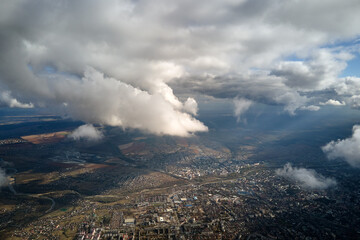 Aerial view from airplane window at high altitude of distant city covered with puffy cumulus clouds...