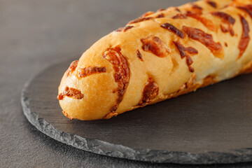 Baguette with baked cheese, on slate stone plate round, dark background, selective focus