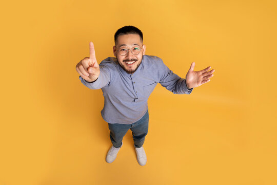 Top view of creative young asian guy in casual outfit pointing finger up
