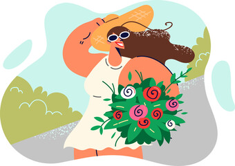 Happy woman with bouquet of wild flowers walks along sidewalk in summer hot park