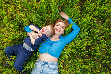 A young mother and her son are lying in the green grass. Family relations of mother and child. A...