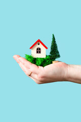 Hand holds a house model on a blue background.