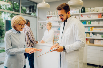 Fototapeta premium Portrait of a male pharmacist helping a senior woman customer in pharmacy