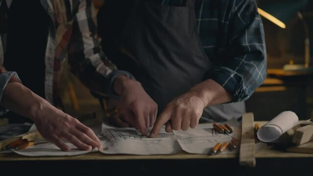 Carpenter, White male woodworker Two fellow workers study drawings of wooden parts for manufacturing In a carpentry workshop A woodworking technician Is in a dark atmospheric room
