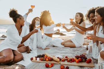 Group of happy women female friends having cozy summer picnic with wine or champagne, having hen party on coastline