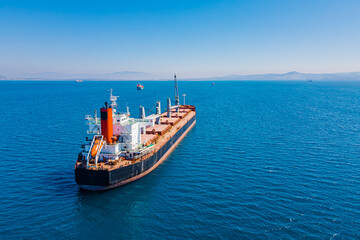 Fototapeta premium Bulk cargo carrier sea ship anchored in Aegean sea waiting entering port, Aerial view