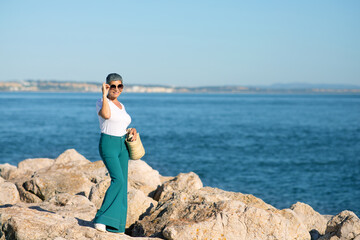 Fototapeta na wymiar European Lady With Gray Hair Posing Wearing Sunglasses At Seaside
