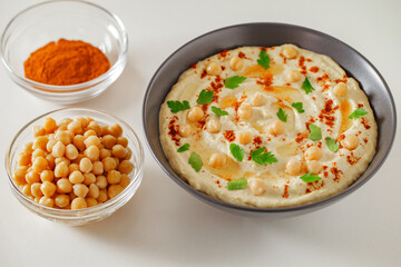 Hummus with chickpeas, oil, spices and herbs in bowl on white table, selective focus